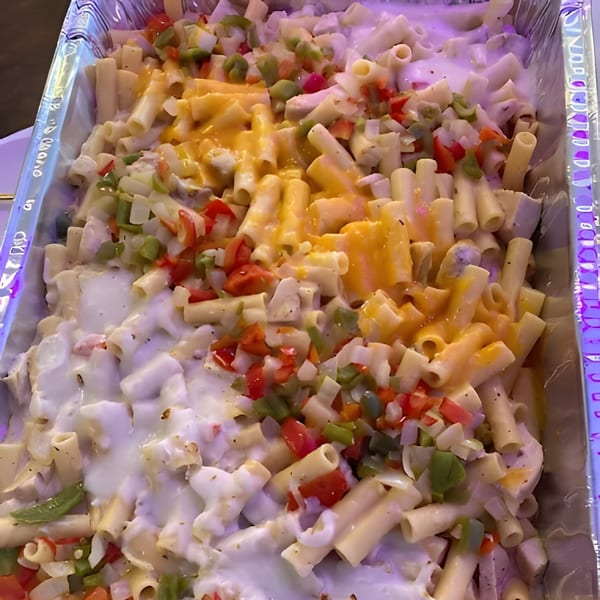 A large tray of creamy pasta with melted cheese, diced red and green peppers, and onions.