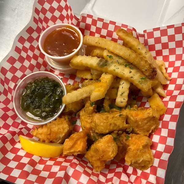 Fried fish and french fries with two dipping sauces and a lemon wedge in a red and white checkered basket.