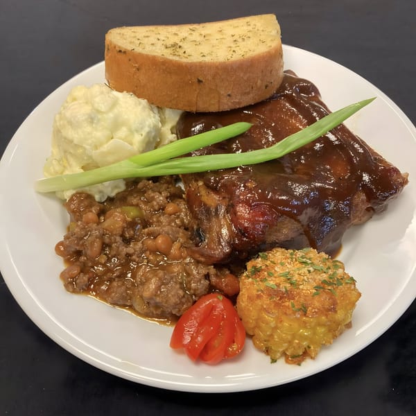 A plate of American cuisine with BBQ ribs, baked beans, potato salad, garlic bread, and a tomato.