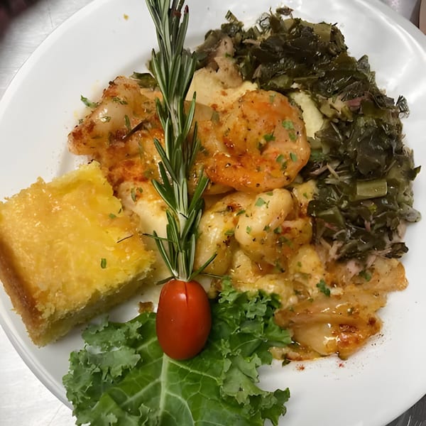 Shrimp and grits with collard greens and cornbread, garnished with rosemary and a cherry tomato.
