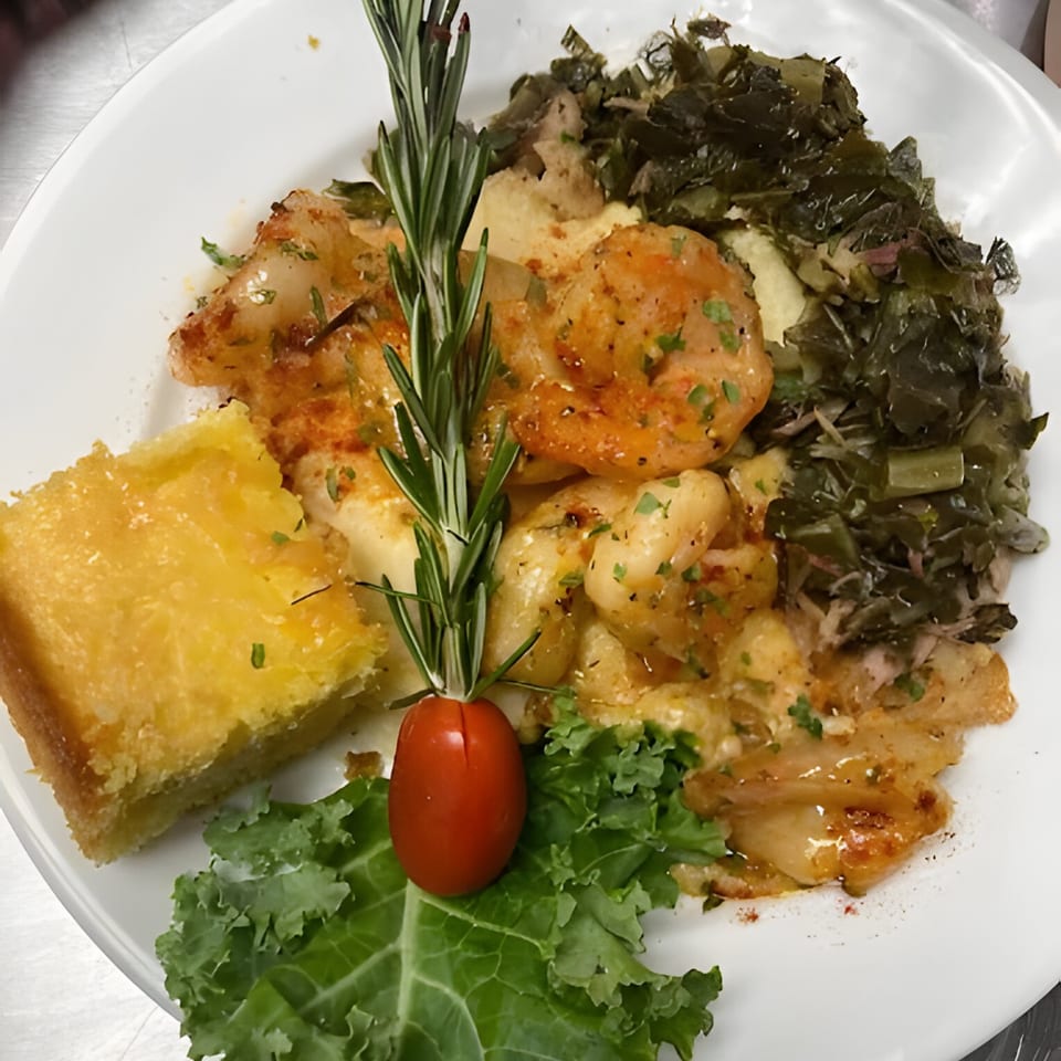 Shrimp and grits with collard greens and cornbread, garnished with rosemary and a cherry tomato.