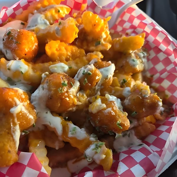 Close-up of golden fried chicken pieces and crinkle-cut fries, drizzled with white sauce and chives.